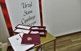 Medale i legitymacje w kolorze bordowym za długoletnie pożycie małżeńskie w tle baner Urzędu Stanu Cywilnego w Starym Kurowie.